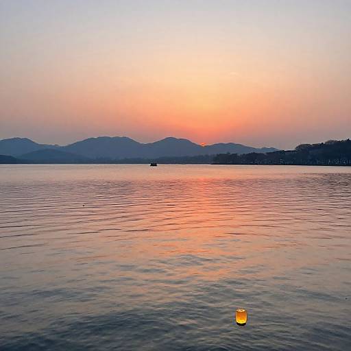 Photograph of a tranquil sunset over a calm lake, with a pink and orange sky reflecting on the water, distant mountains, and a single yellow buoy