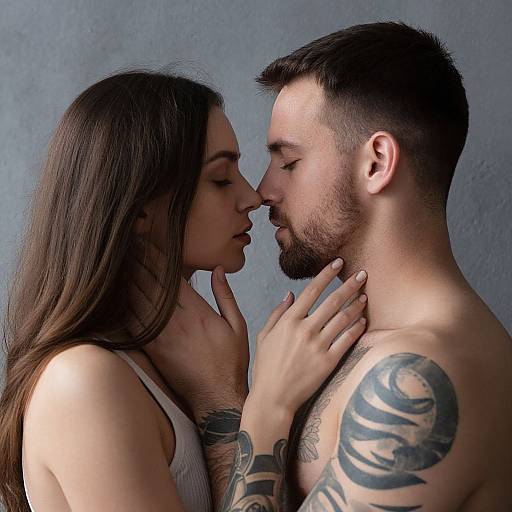 Photograph of a tattooed, bearded man and woman with long brown hair, leaning close, eyes closed, hands touching, against a gray wall