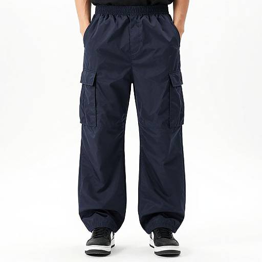 Photograph of a person wearing black cargo pants with pockets, black elastic waistband, and black sneakers, standing against a plain white background.