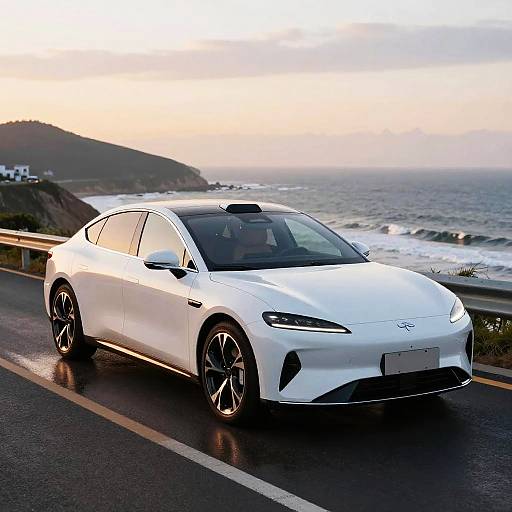 Photograph of a sleek, white Hyundai sports sedan with black rims parked on a wet coastal road at sunset, ocean waves in background.