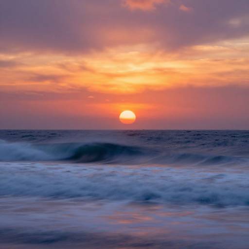 Photograph of a vibrant sunset over the ocean, with orange and pink clouds, a bright sun near the horizon, and blue, white-capped waves