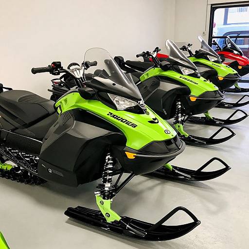 Photograph of three bright green and black snowmobiles lined up in a well-lit, white-walled garage with a computer screen in the background