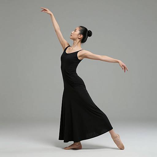 Photograph of a slender, dark-haired woman in a black, sleeveless, floor-length dress, ballet pointe shoes, graceful ballet pose against a