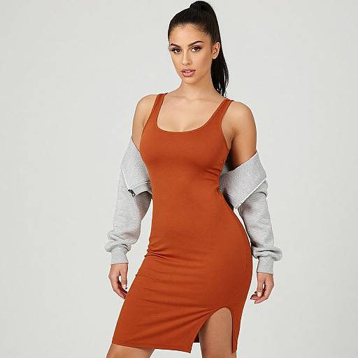 Photograph of a woman with dark hair in a high ponytail, wearing a tight, orange, sleeveless dress with a side slit, and a