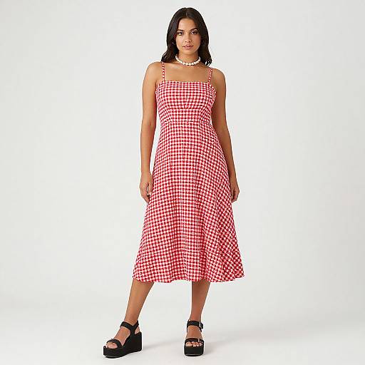 Photograph of a woman with medium skin tone, black hair, wearing a red gingham sleeveless dress, white necklace, and black platform sandals,