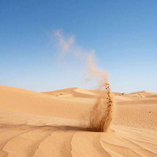 Photograph of a sand dune with a powerful sand eruption, under a clear, bright blue sky; golden sand swirls gracefully.