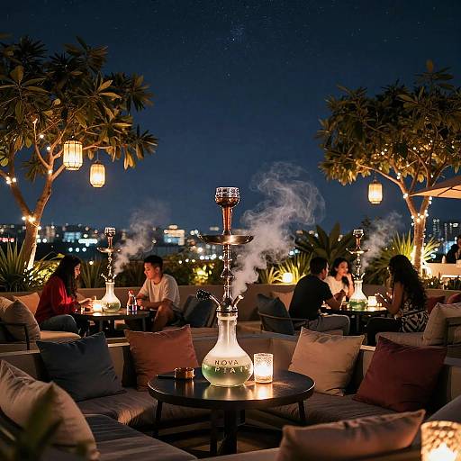 Nighttime rooftop lounge with lit lanterns, smoke-filled hookahs, and groups of people sitting on cushioned sofas, surrounded by palm trees and