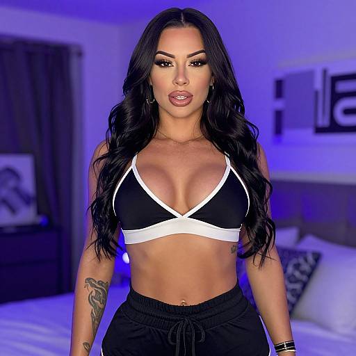 Photograph of a fit woman with long black hair, tan skin, large breasts, black and white sports bra, black pants, tattoos, in a