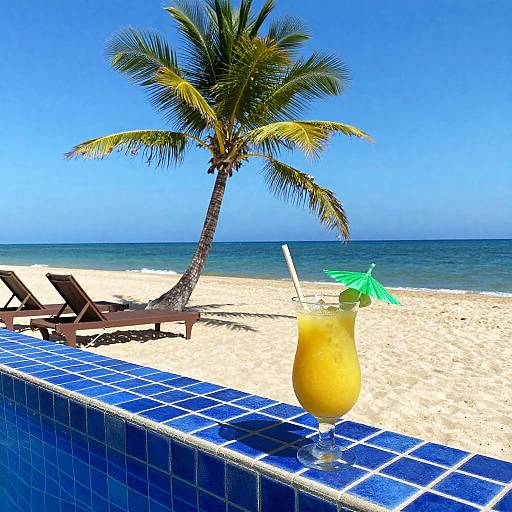 Photograph of a tropical beach with a yellow cocktail garnished with a green umbrella on a blue-tiled pool edge, palm tree, and two empty