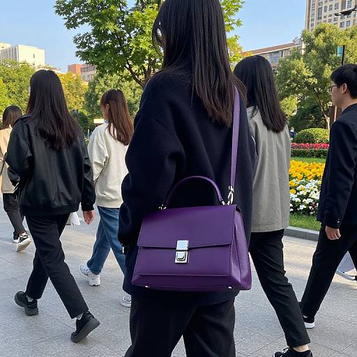 Photograph of five Asian women with long black hair, wearing black and gray jackets, walking in a sunlit urban park, one carrying a purple hand