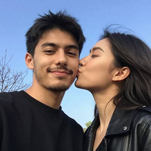 Photograph of a smiling Indian man with short black hair and a mustache, being kissed on the cheek by a woman with long black hair wearing a