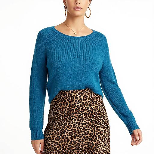Photograph of a woman wearing a blue knitted sweater and a leopard-print skirt, standing against a plain white background.
