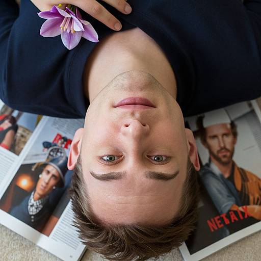Close-up photograph of a young man with short brown hair, blue eyes, and fair skin, lying upside down, wearing a black shirt, with purple