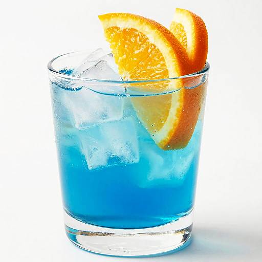 Photograph of a clear glass with vibrant blue cocktail, ice cubes, and a thick orange slice garnish, against a white background.