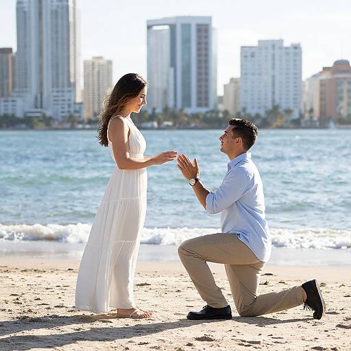 Photograph of a man kneeling on a sunny beach, proposing to a woman in a white dress, with city skyscrapers in the background.