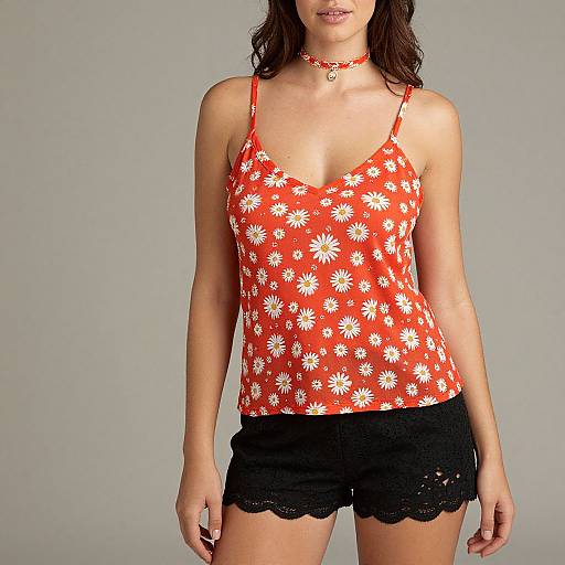 Photograph of a woman with medium skin tone wearing a red, white daisy-patterned camisole, black lace shorts, and a red ch