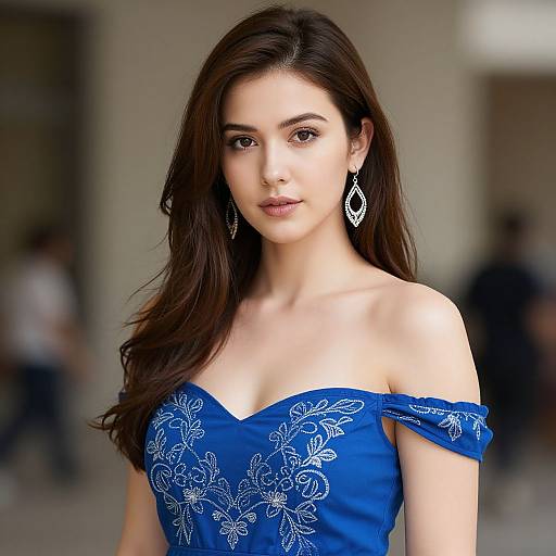 Photograph of a young woman with long dark brown hair, wearing an off-shoulder blue dress with white floral embroidery, and silver teardrop