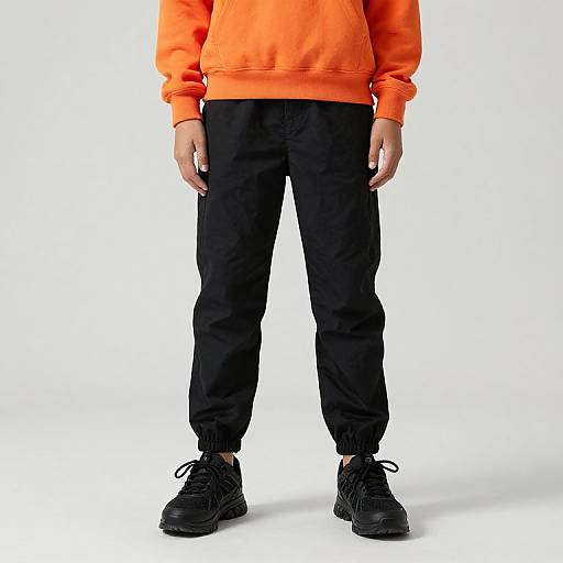 Photograph of a person wearing a bright orange hoodie, black joggers, and black sneakers, standing against a plain white background.