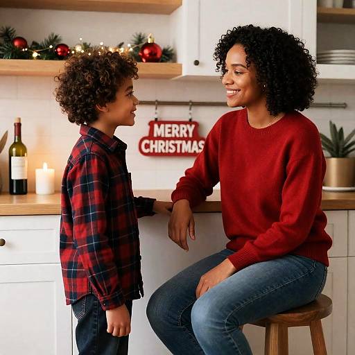 Photograph of a smiling Black woman with curly hair in a red sweater and jeans, talking to a curly-haired Black boy in a plaid shirt,
