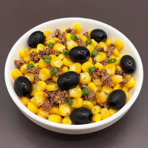Photograph of a white bowl filled with yellow corn, black olives, crumbled brown meat, and chopped green onions on a dark background.