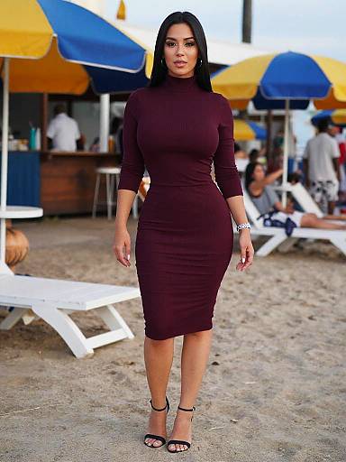 Photograph of a curvy Latina woman with long black hair in a form-fitting, long-sleeve maroon dress and black heels, standing