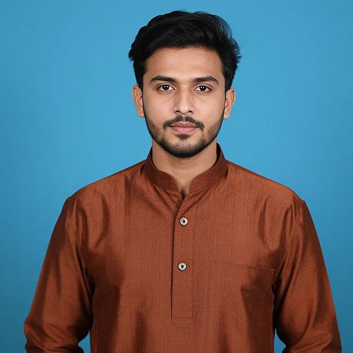 Photograph of a South Asian man with medium brown skin, black hair, and beard, wearing a rust-colored button-up shirt, against a bright blue