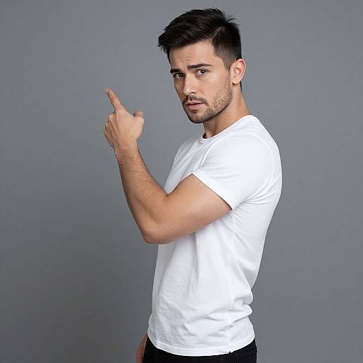 Photograph of a handsome, light-skinned man with short black hair, trimmed beard, wearing a white t-shirt, pointing up with his right index