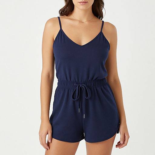 Photograph of a woman in a navy blue, spaghetti-strap, V-neck romper with a tie waist, standing against a plain white background.