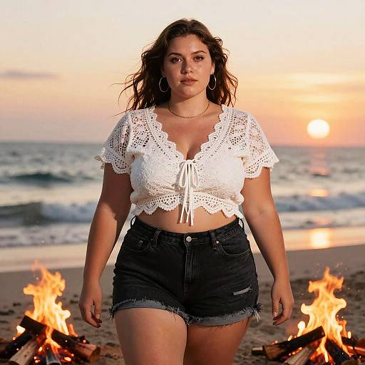 Photograph of a curvy woman with long brown hair, wearing a white lace crop top and black denim shorts, standing in front of a beach sunset