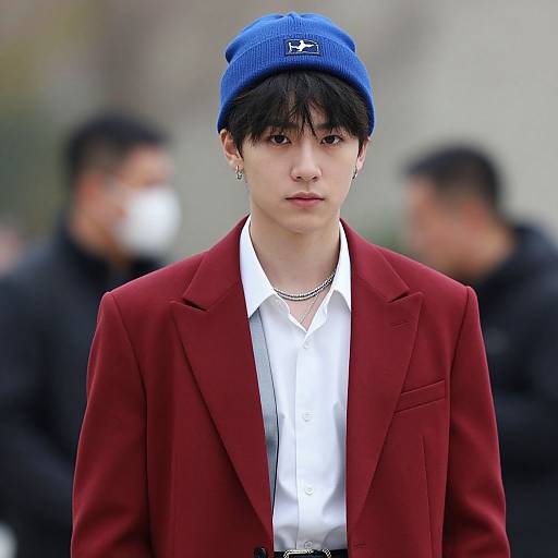 Photograph of a young Asian man with pale skin, black hair, wearing a blue beanie, red blazer, white shirt, and silver necklace