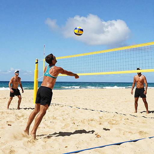 Photograph of three shirtless men playing beach volleyball on a sunny sandy beach with a clear blue sky and ocean in the background. One man spikes the
