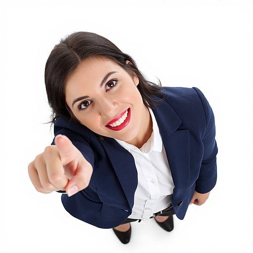 Photograph of a smiling woman with dark hair, red lipstick, and black suit, pointing towards the camera from an overhead angle.