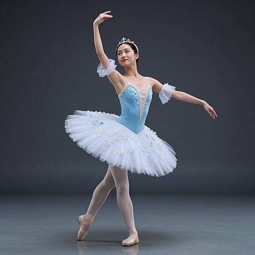 Photograph of a young Asian ballerina in a blue and white tutu, tiara, and pointe shoes, gracefully dancing against a dark