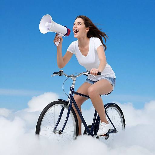Photograph of a smiling, dark-haired woman in a white t-shirt and denim shorts, riding a black bicycle through fluffy clouds, holding a white meg