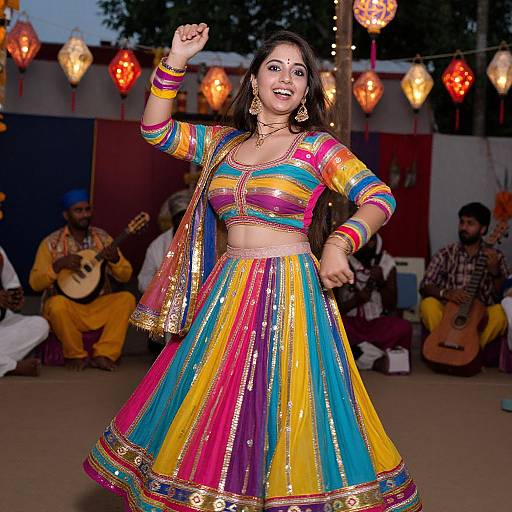 Photograph of a smiling Indian woman dancing in vibrant, colorful traditional attire, surrounded by musicians and string lights at dusk.