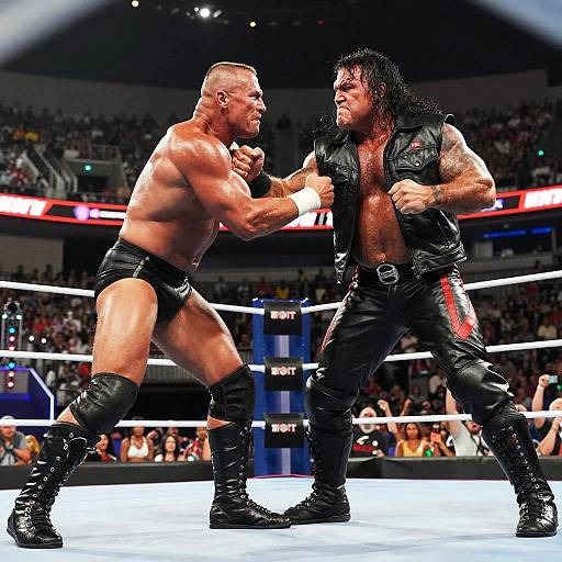 Photograph of two muscular men in a wrestling ring, one with a bald head and black trunks, the other with long black hair and a black