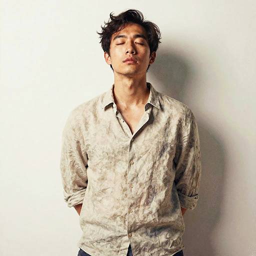 Photograph of an Asian man with tousled black hair, closed eyes, and a neutral expression, wearing a textured, light gray, button-down shirt