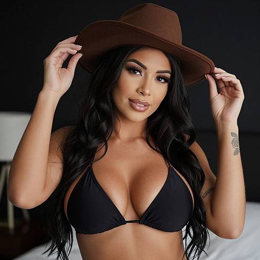 Photograph of a woman with long black hair, tan skin, large breasts in a black bikini top, and a brown cowboy hat, smiling against a
