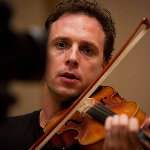 Close-up photograph of a focused, middle-aged man with short, dark hair playing a violin, warm lighting highlighting his expressive face.