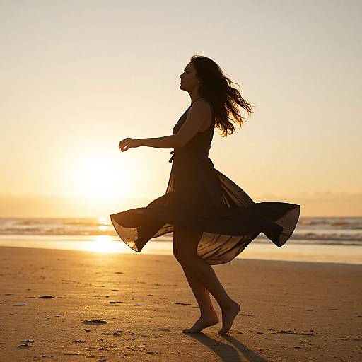 Silhouetted woman in flowing black dress dancing on golden sandy beach at sunset, with sun low on horizon, ocean waves in background. Photograph.