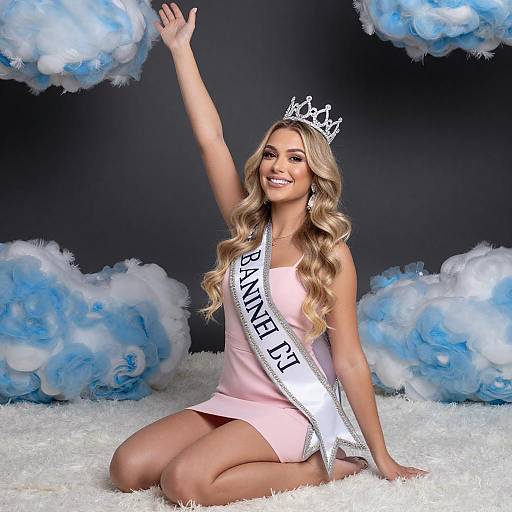 Photograph of a smiling blonde woman with wavy hair, wearing a silver crown, pink dress, and 