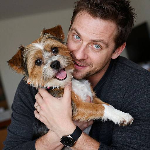 Photograph of a smiling, blue-eyed white man with short brown hair holding a small, brown and white terrier with tongue out.