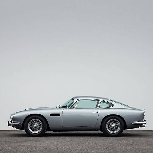 Photograph of a sleek, silver classic sports car in profile, with wire-spoke wheels, against a minimalistic white-to-light-blue gradient background.