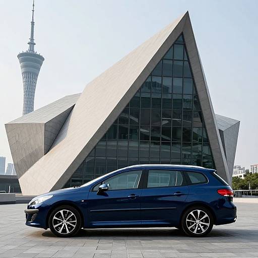 Photograph of a modern, geometric glass building with sharp, triangular angles in the background, featuring a blue compact car in the foreground and a distant TV