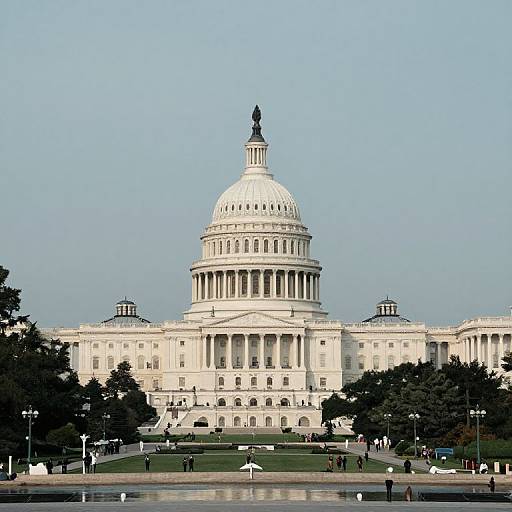 Photograph of the United States Capitol with its white dome and classical columns, surrounded by trees and people in the foreground.