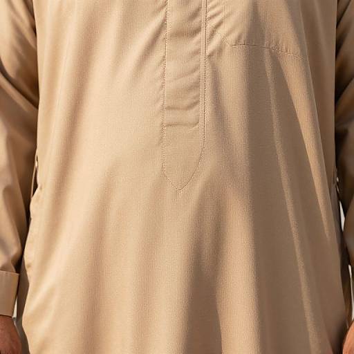 Close-up photograph of a beige, long-sleeved, buttoned shirt with a single, slightly curved pocket, capturing the fabric's texture and subtle