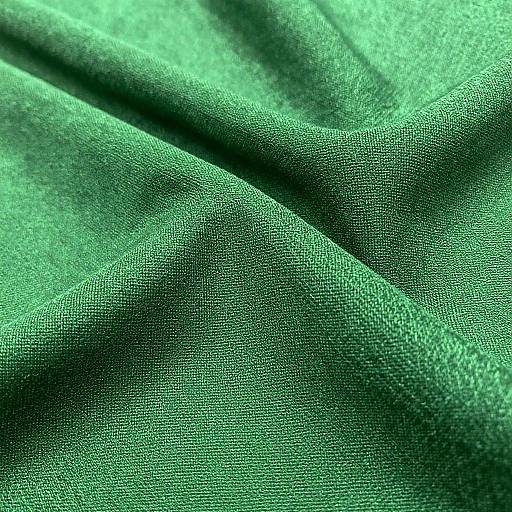 Close-up photograph of textured, green fabric with intricate patterns, shadows, and folds, highlighting a rich, detailed, and slightly shimmering surface.