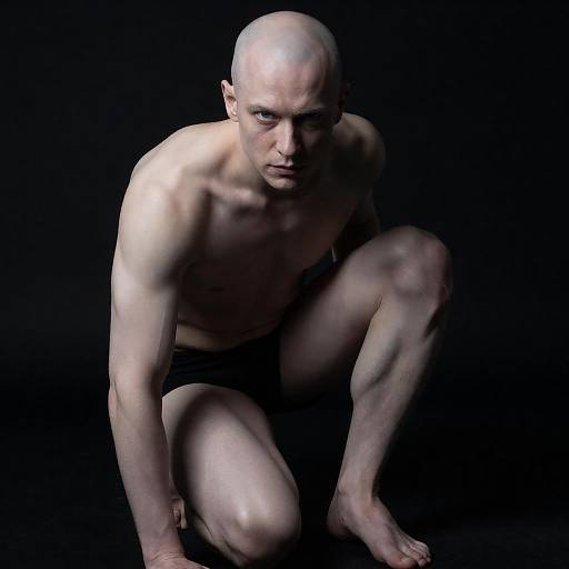 Crouching Bald Muscular Man with Intense Blue Eyes