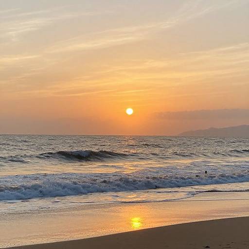 Photograph of a serene beach at sunset: orange sun sets over calm, gently rippling ocean waves, reflecting on wet sand, with a hazy
