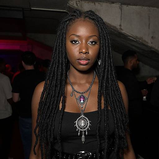 Photograph of a dark-skinned Black woman with long braids, wearing a black strapless top, intricate jewelry, and a confident expression, standing